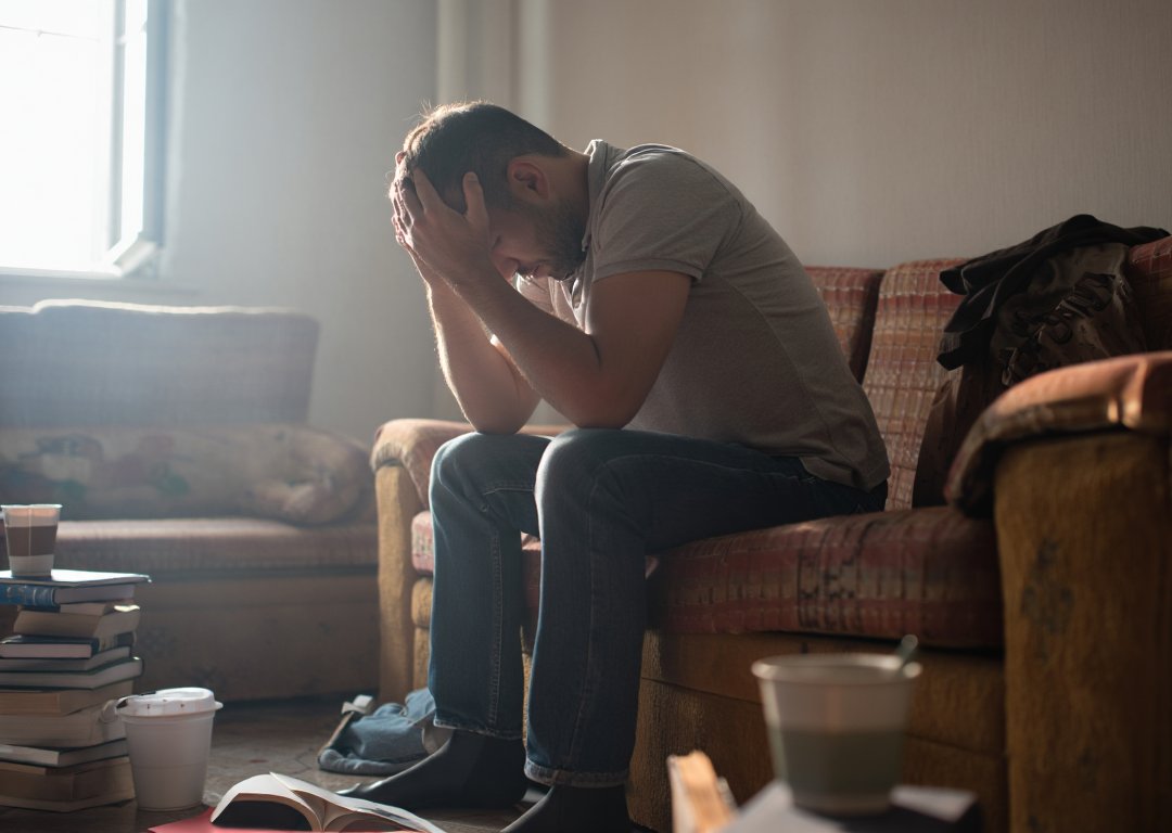 Мужчина сидит на диване и держится за голову